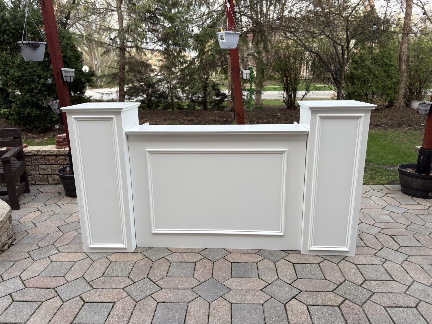 White panel-front event bar with matching pedestal columns, set up on a paver patio