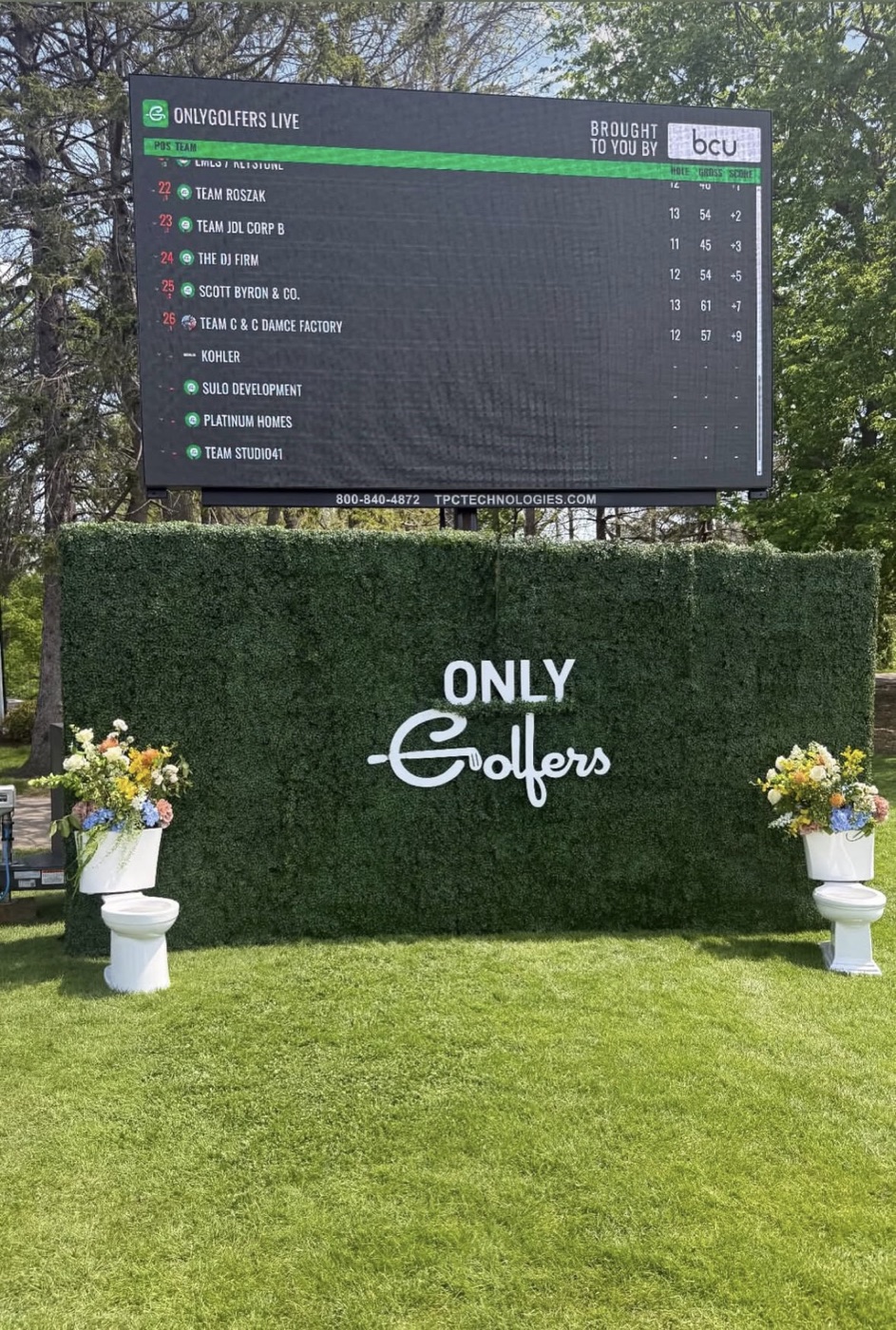 “Only Golfers” greenery hedge wall with a monogram logo and live leaderboard screen